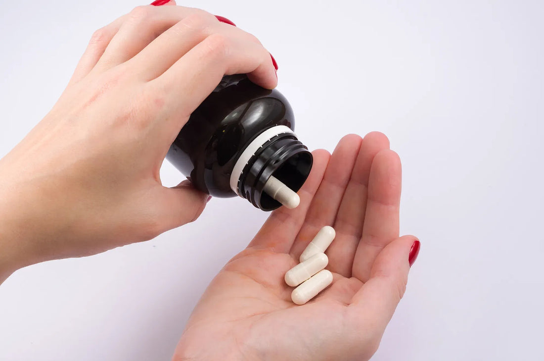Woman pouring magnesium supplement capsules from a bottle into the palm of her hand on a white background.